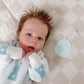 Newborn baby wearing a white sweater with blue patterns, lying on a checkered blanket.